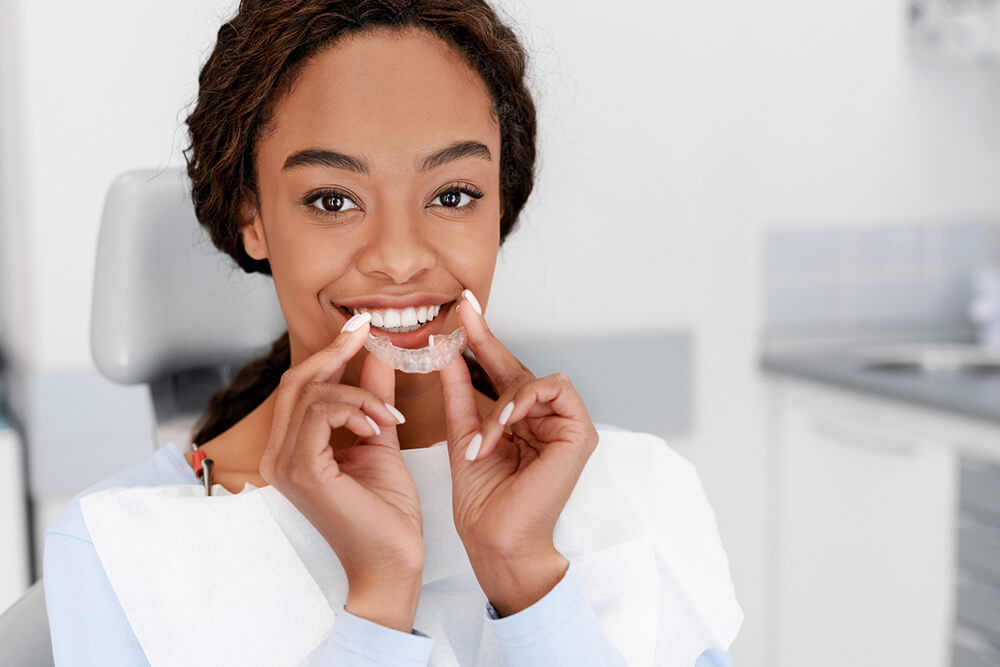 woman smiling as she is about place upper row of clear aligners onto teeth